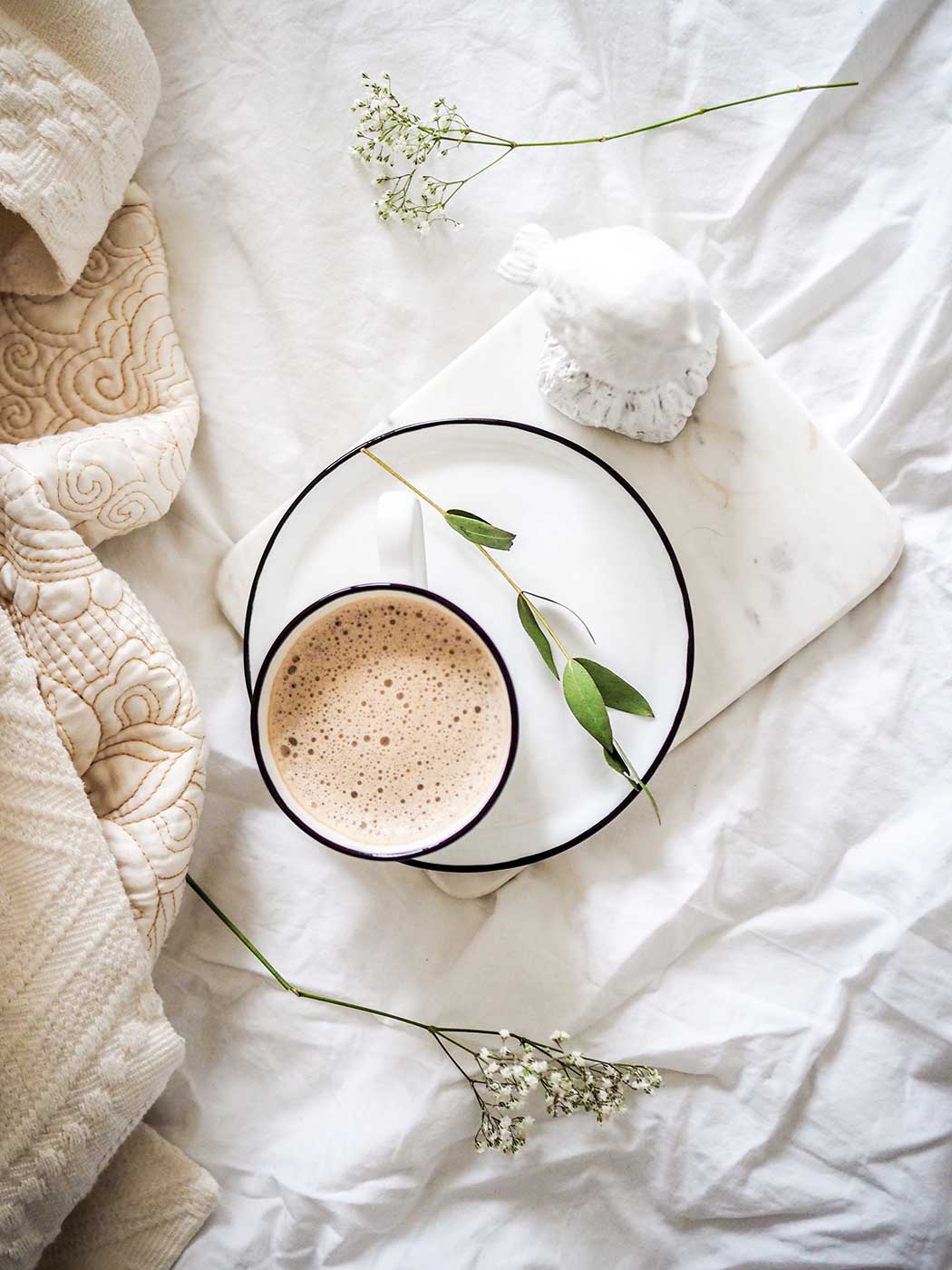 Flat lay photography featuring coffee and flowers on white bedsheets.