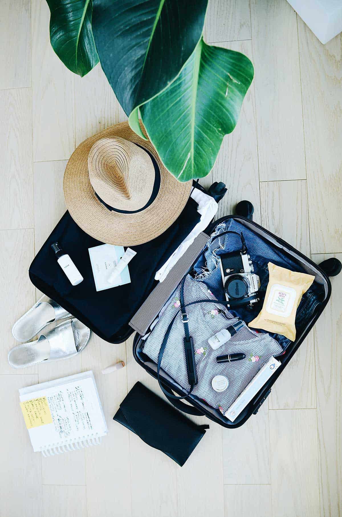 suitcase flatlay with clothes and hat