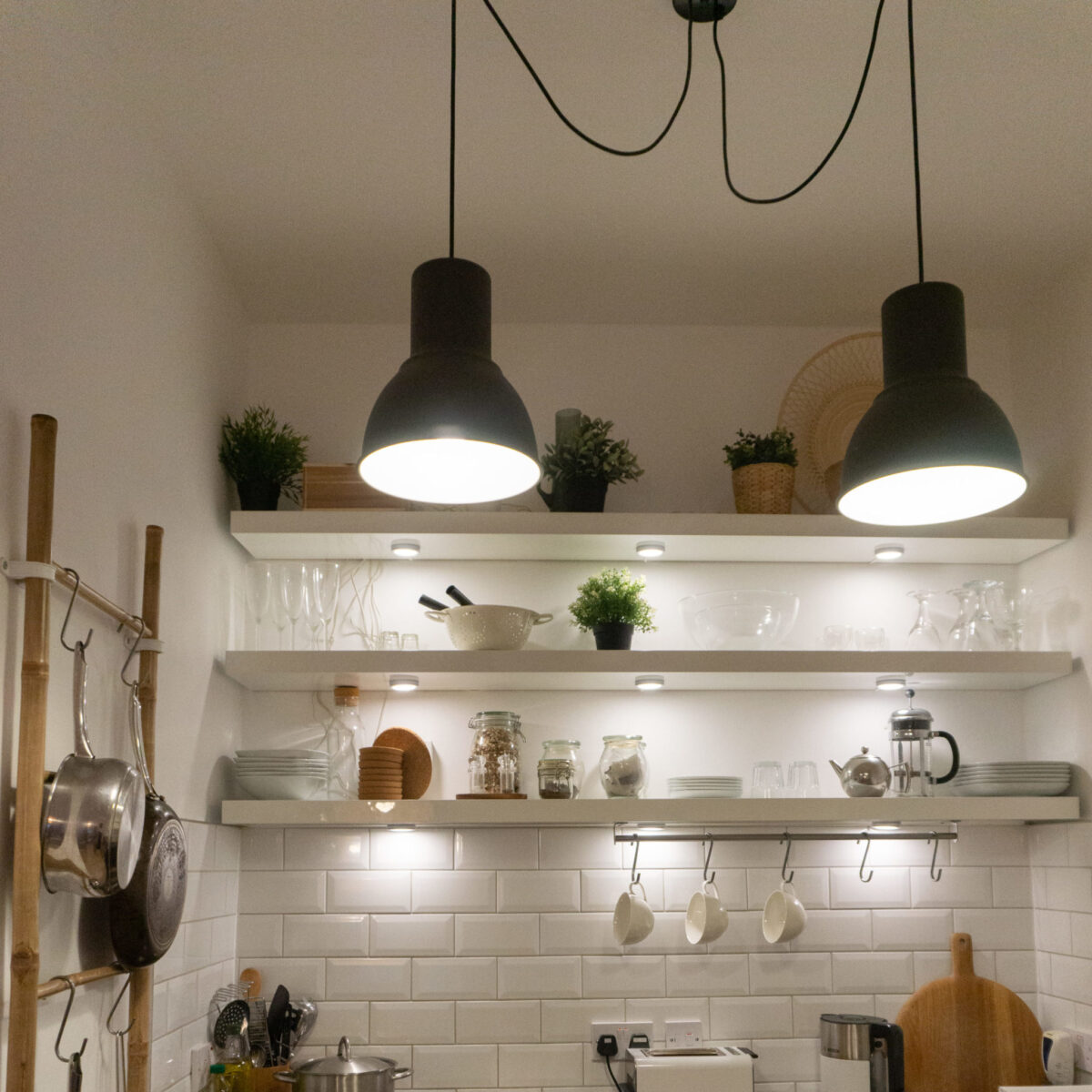 Modern open shelved kitchen with utensils, hanging lights and white tiles.