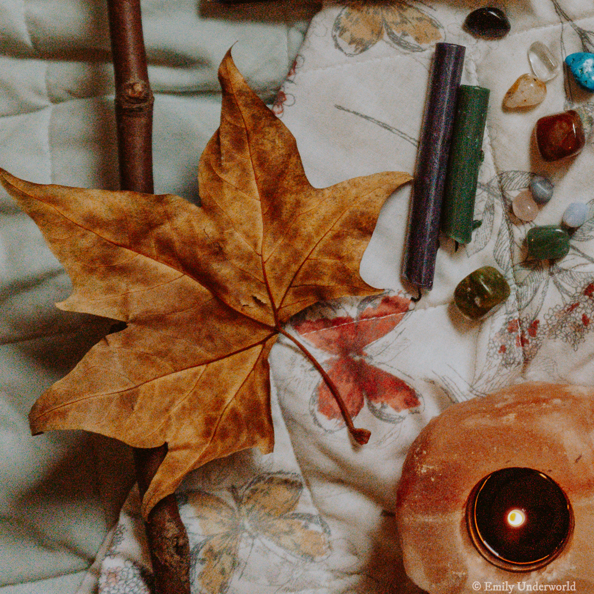 a flat lay of autumnal objects, including a fallen leaf, candles, crystals and a stick.