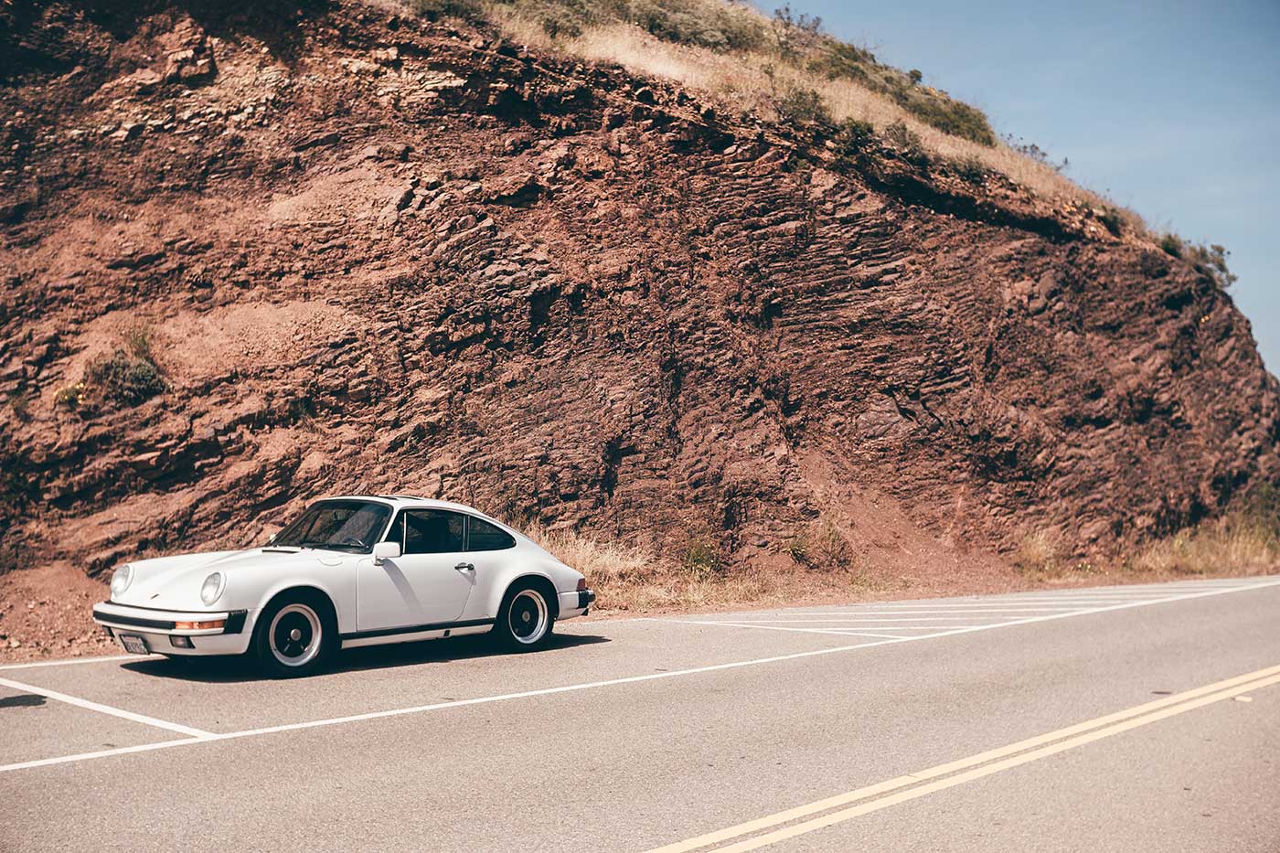 A beautiful white Classic car, driving beside a cliff.