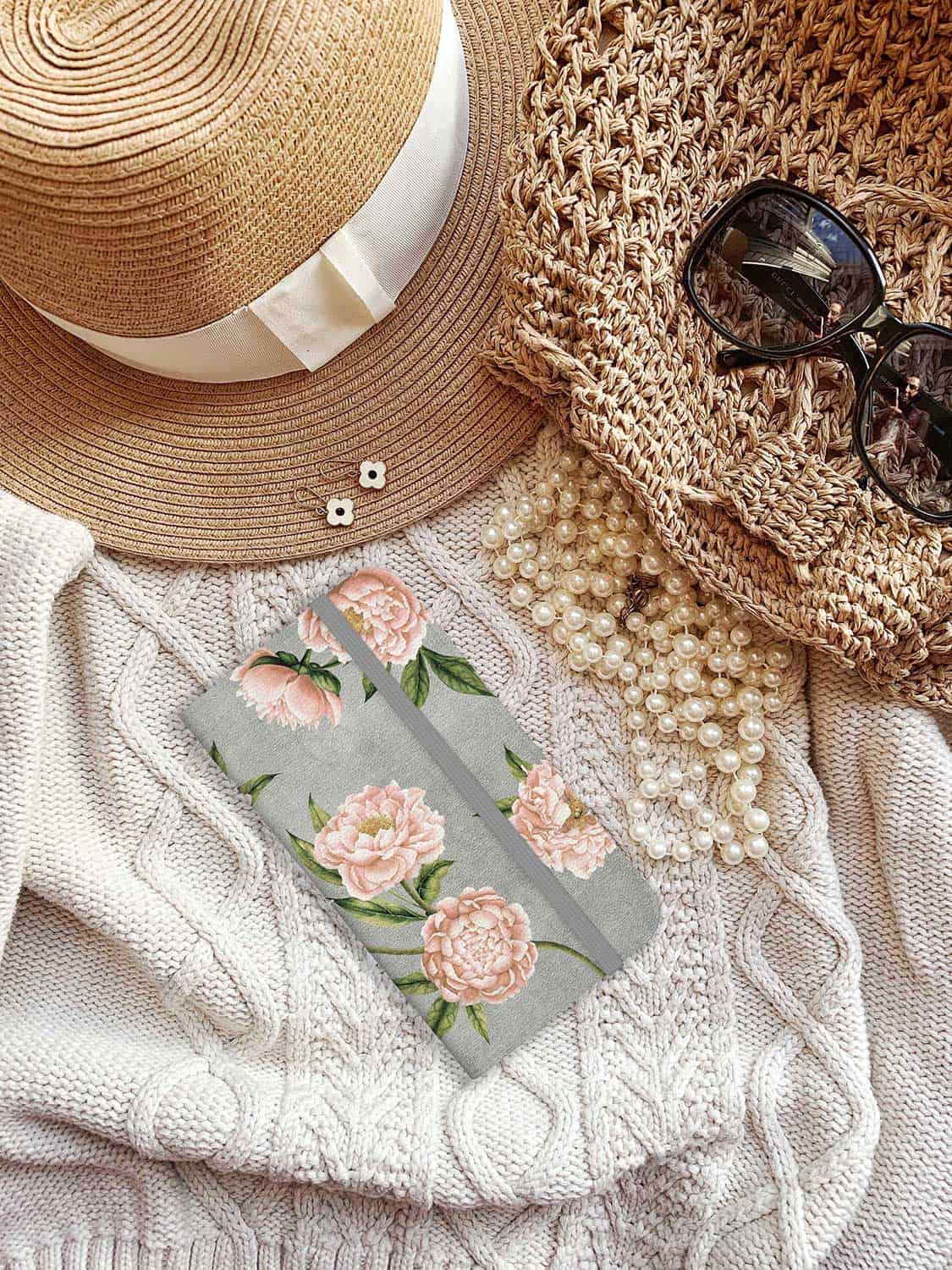 Fashion accessories flat lay: sunglasses, straw hat, earrings, jumper, floral phone case.