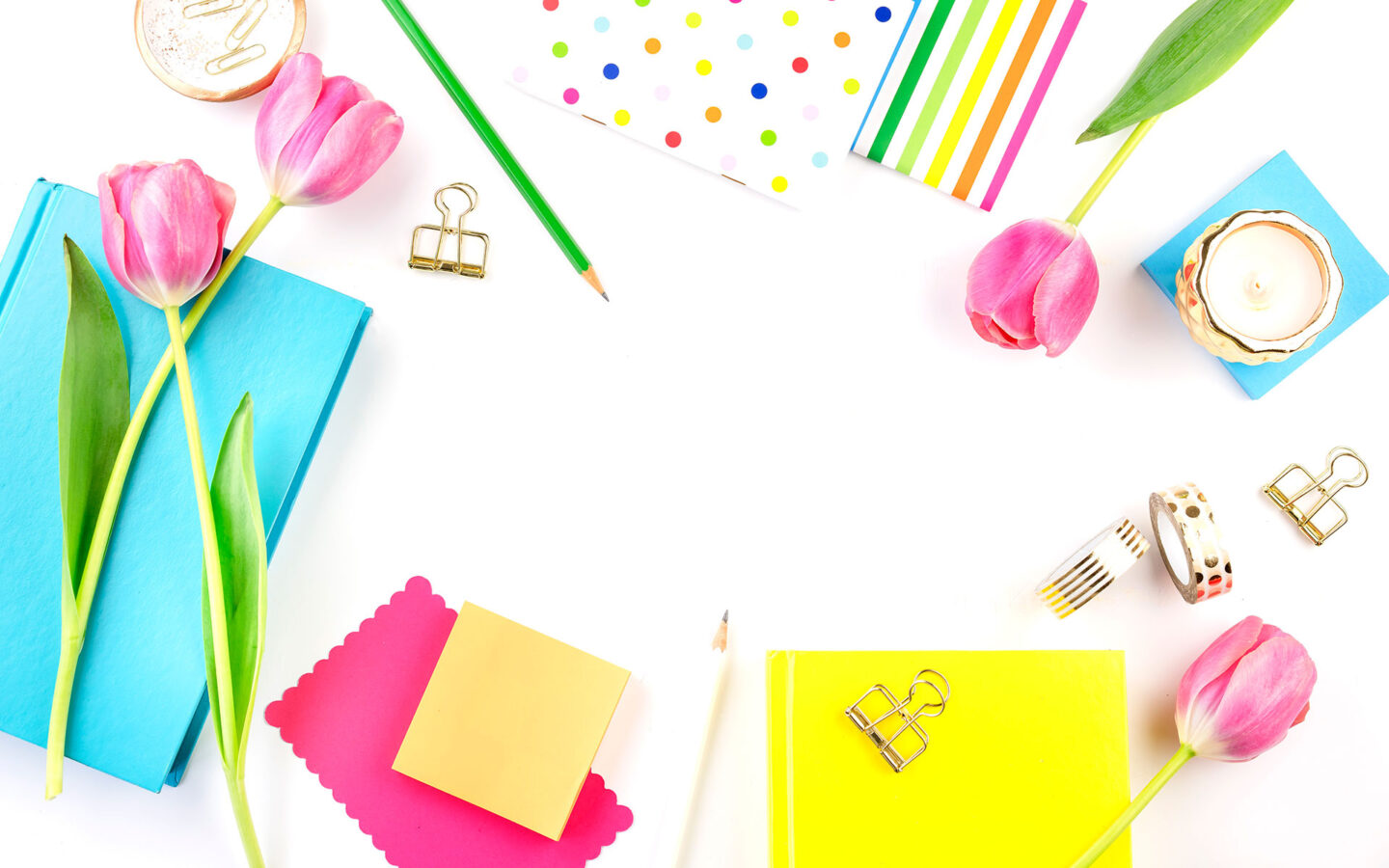 brightly coloured stationery, candles and tulips on a white desk.