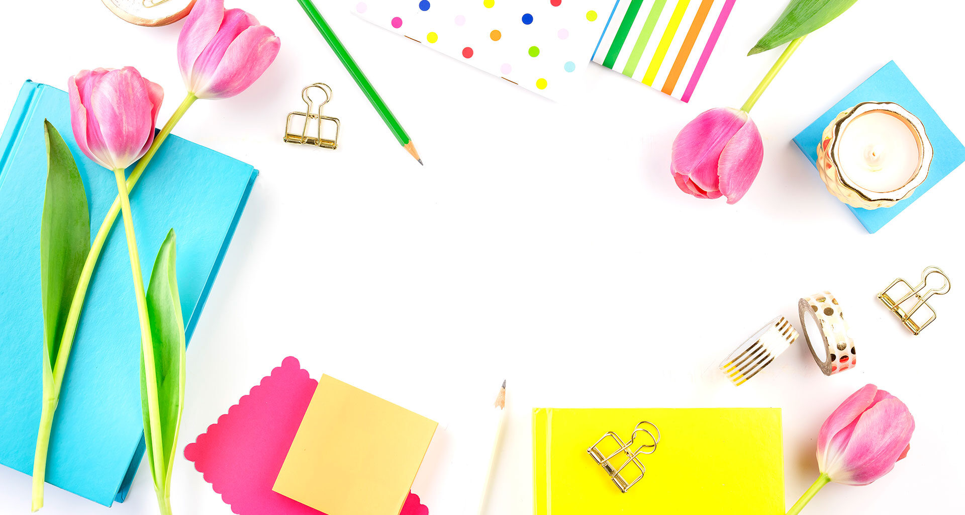 brightly coloured stationery, candles and tulips on a white desk.