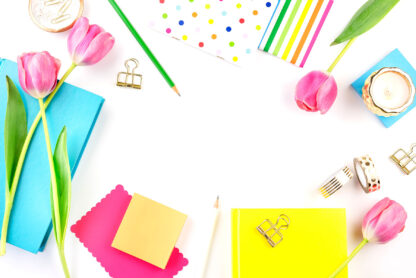 brightly coloured stationery, candles and tulips on a white desk.