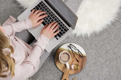 woman typing on laptop with coffee and glasses on side table.