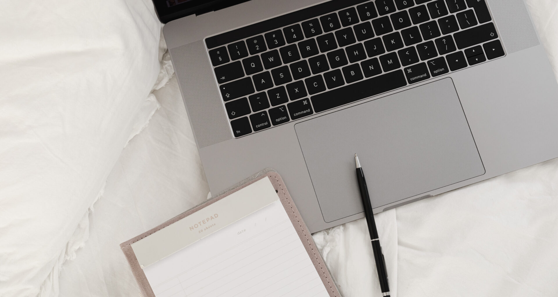 working with a laptop in bed white cotton bedding blank notebook pen