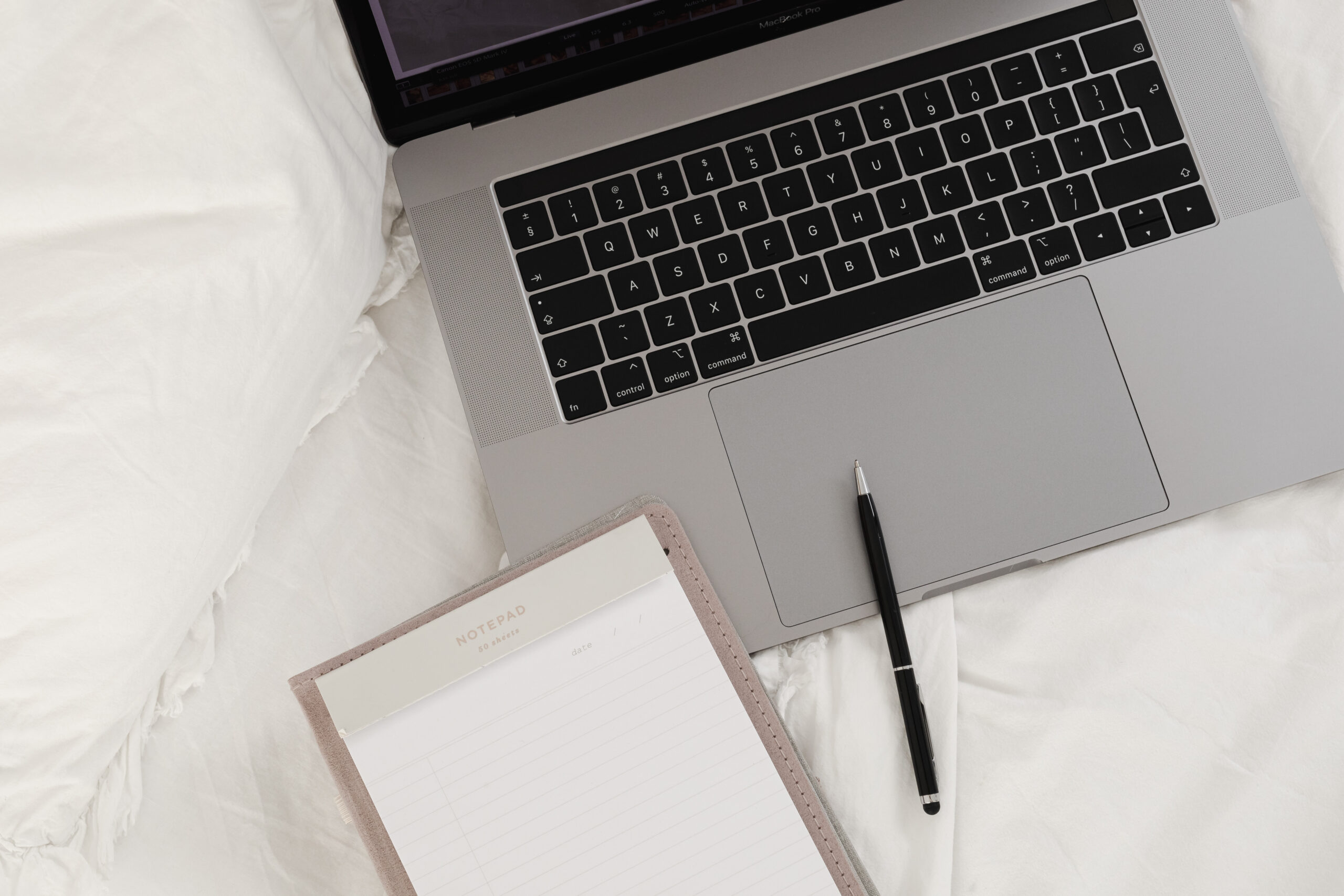 working with a laptop in bed white cotton bedding blank notebook pen
