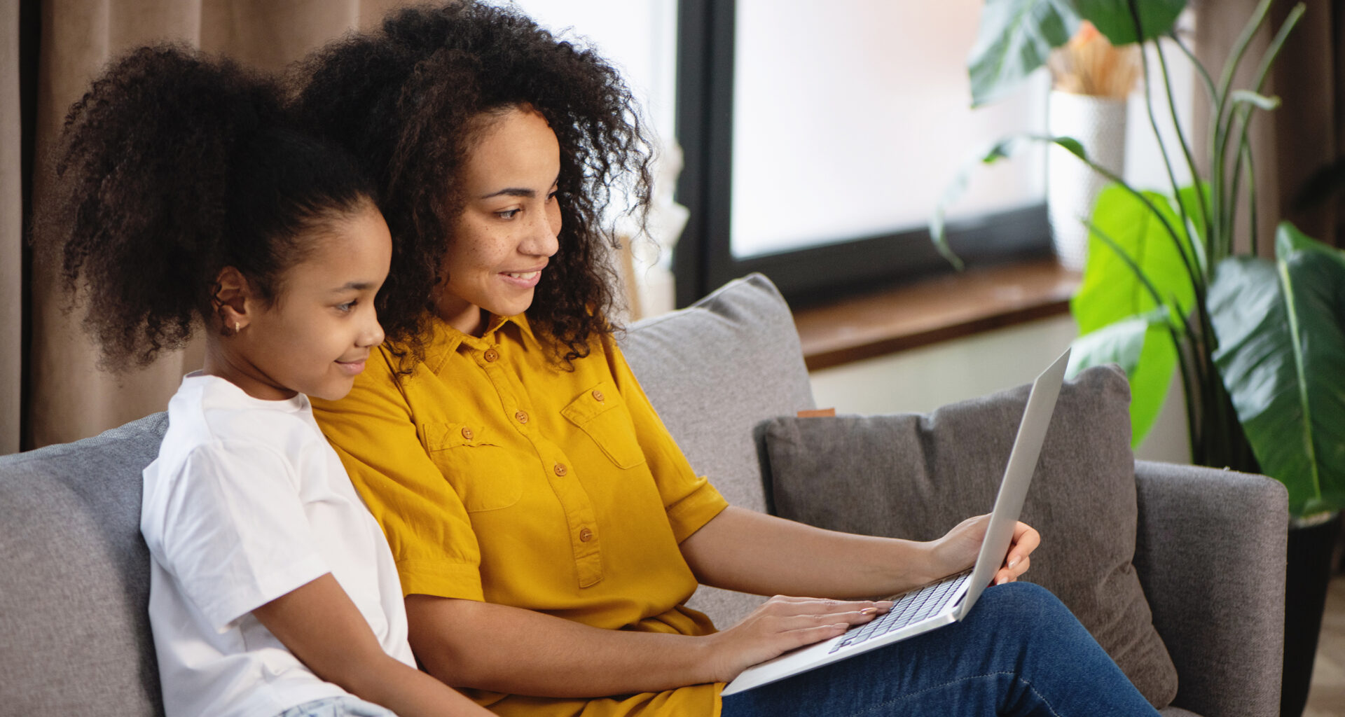 Woman and daughter looking at laptop on sofa.