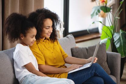 Woman and daughter looking at laptop on sofa.