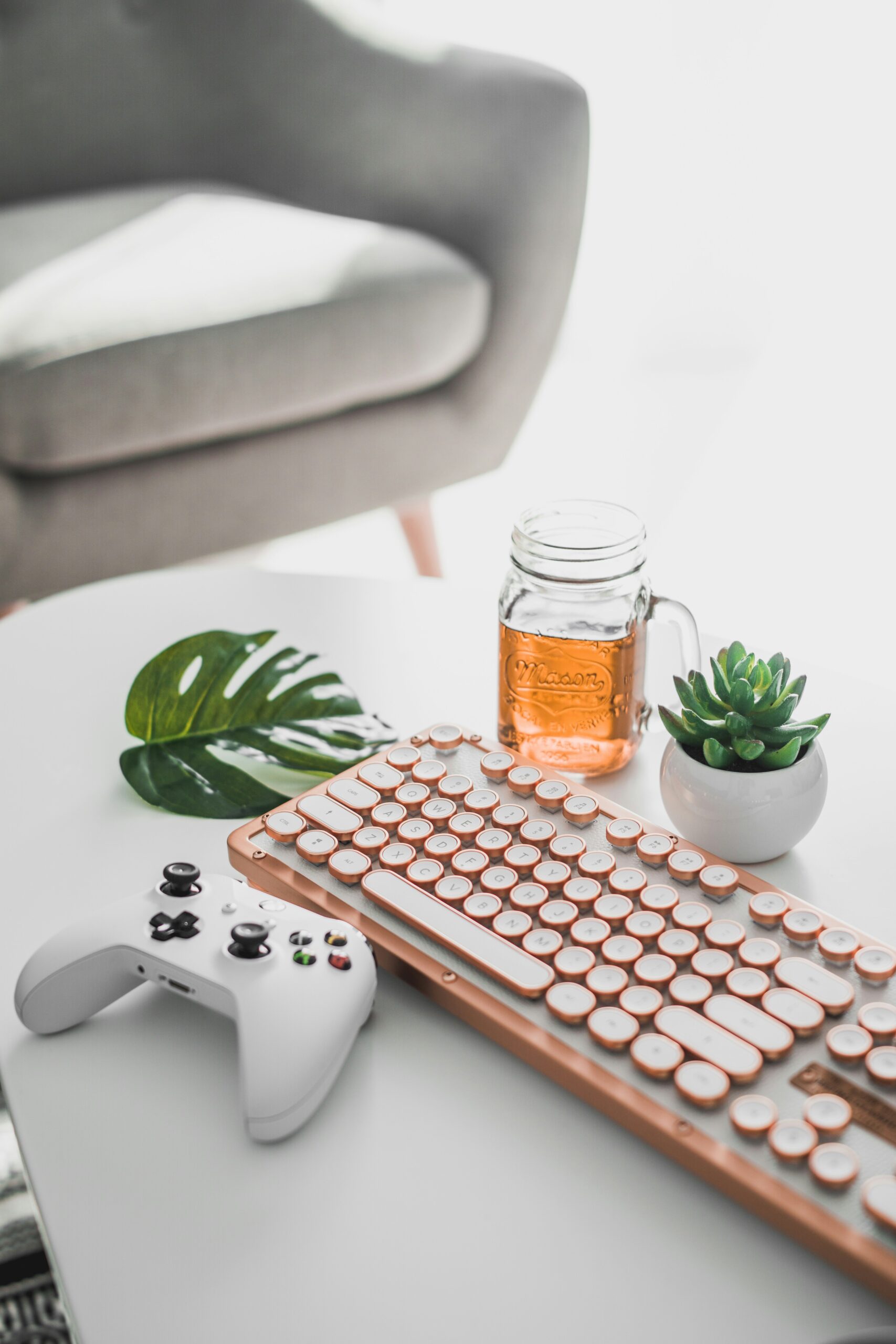 rose gold keyboard, white xbox controller, plants and mason jar with drink.