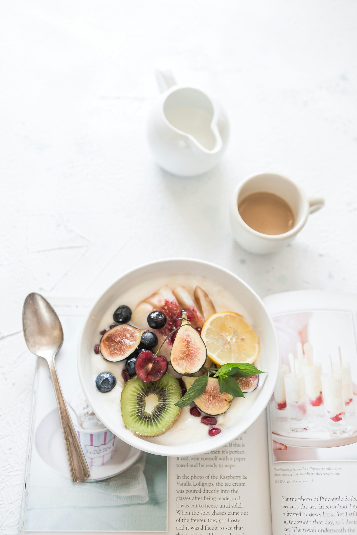 bowl of fruit and yoghurt for breakfast with a cup of tea and a book.
