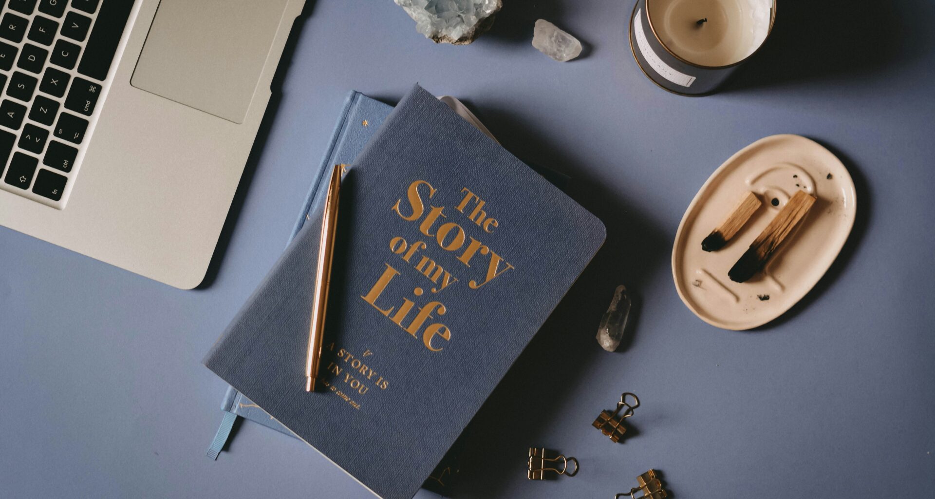 story of my life journal on a navy blue desk with laptop, candle, crystal and other objects.