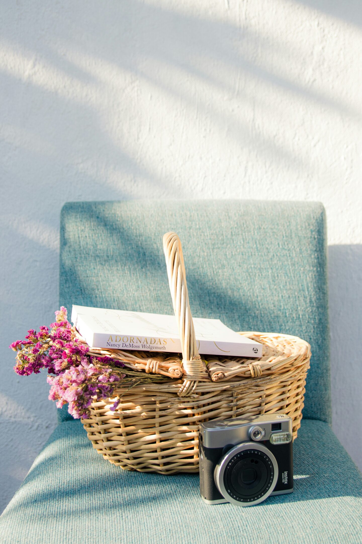 wicker basket holding flowers and a book on a chair.
