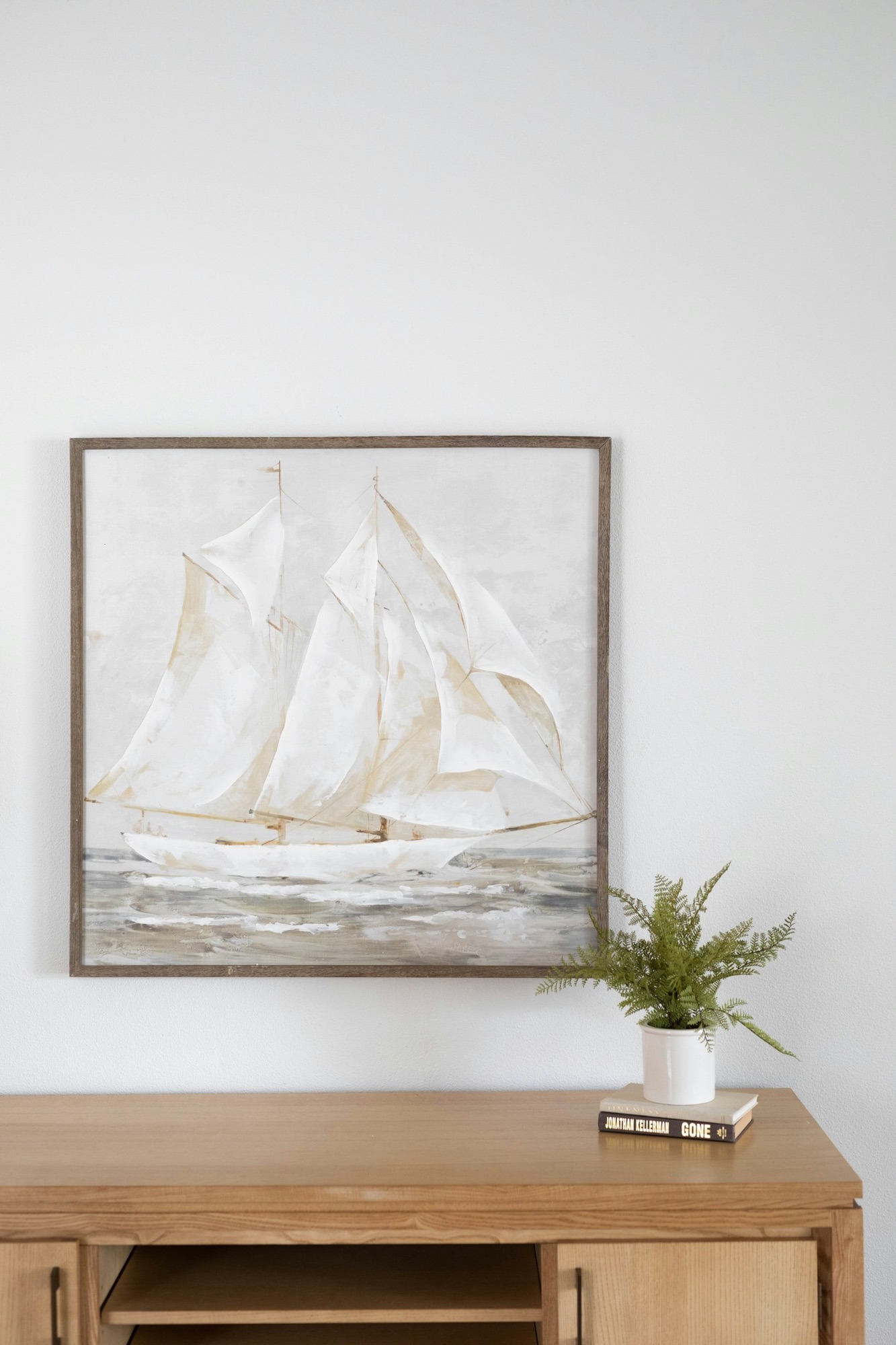 minimalist home decor: a paitning of a ship, a plant and a book on a wooden side unit.