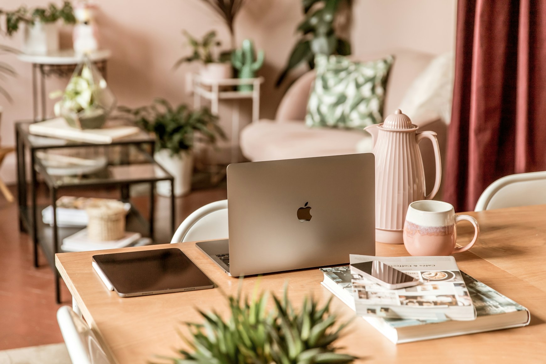 a feminine workspace setup in a living room filled with pastel pinks and plants.