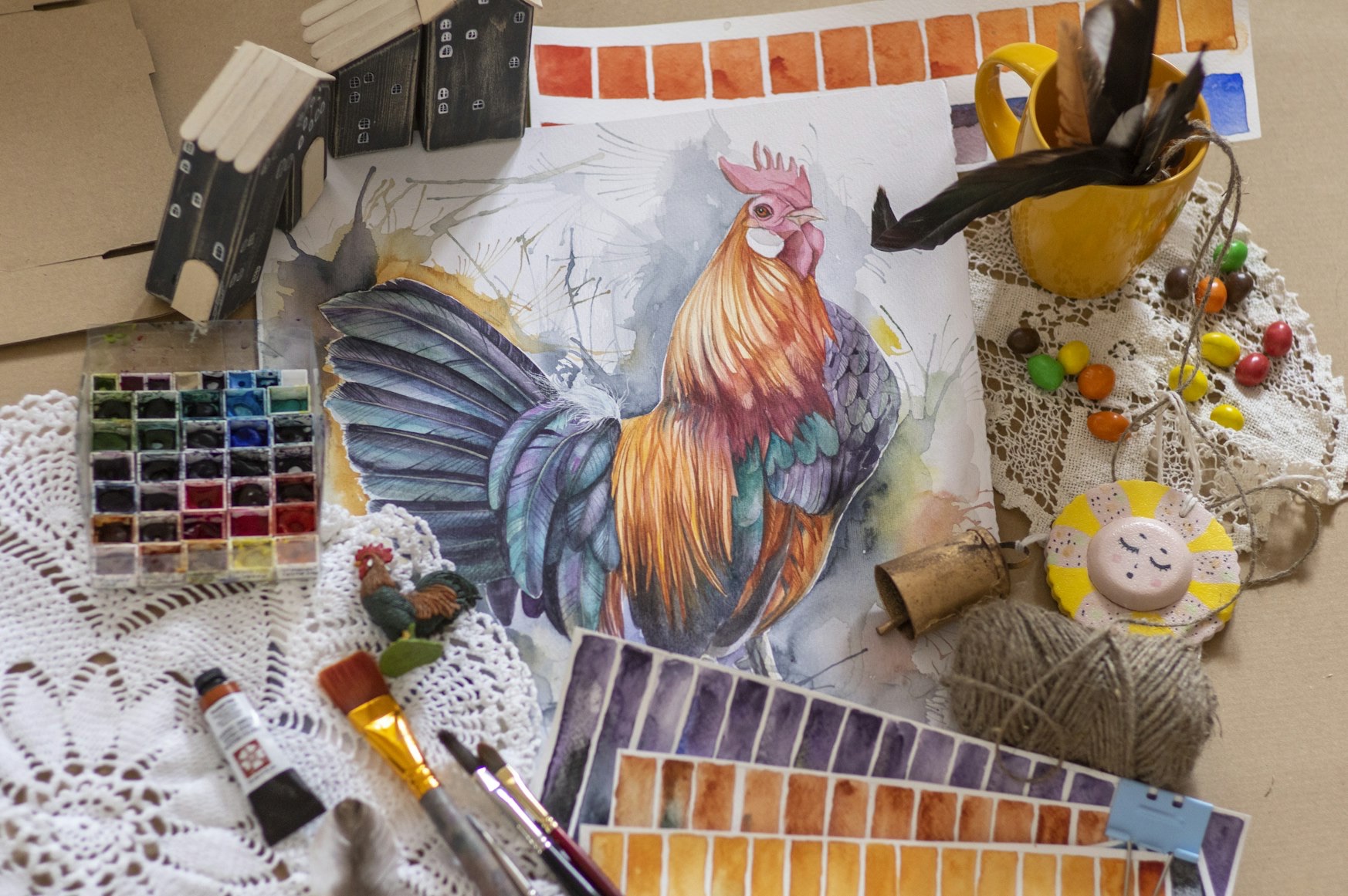watercolour painting of a cockerel, surrounded by paints, brushes and other art supplies.