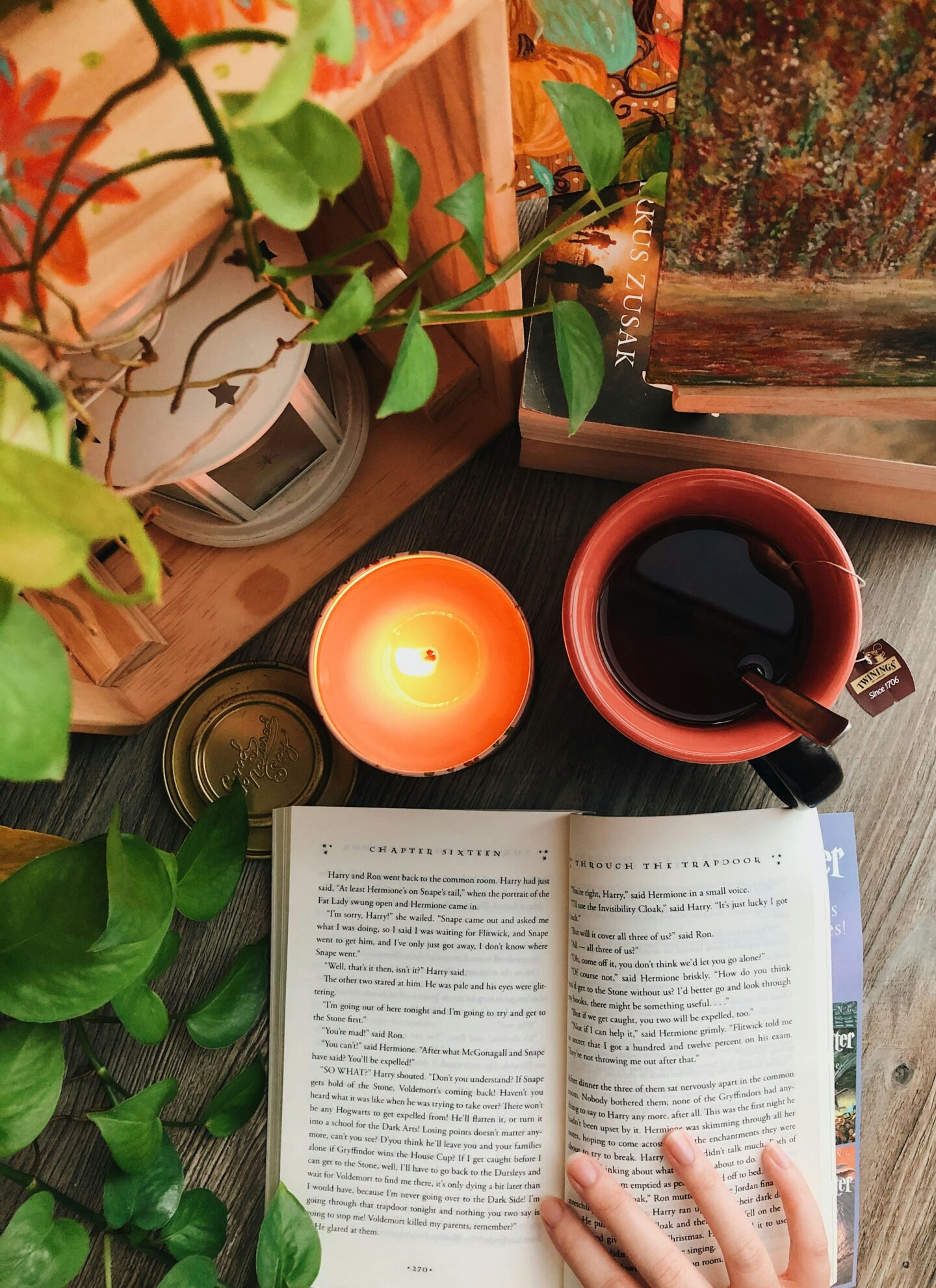open harry potter book on desk with plants, candle and cup of tea.