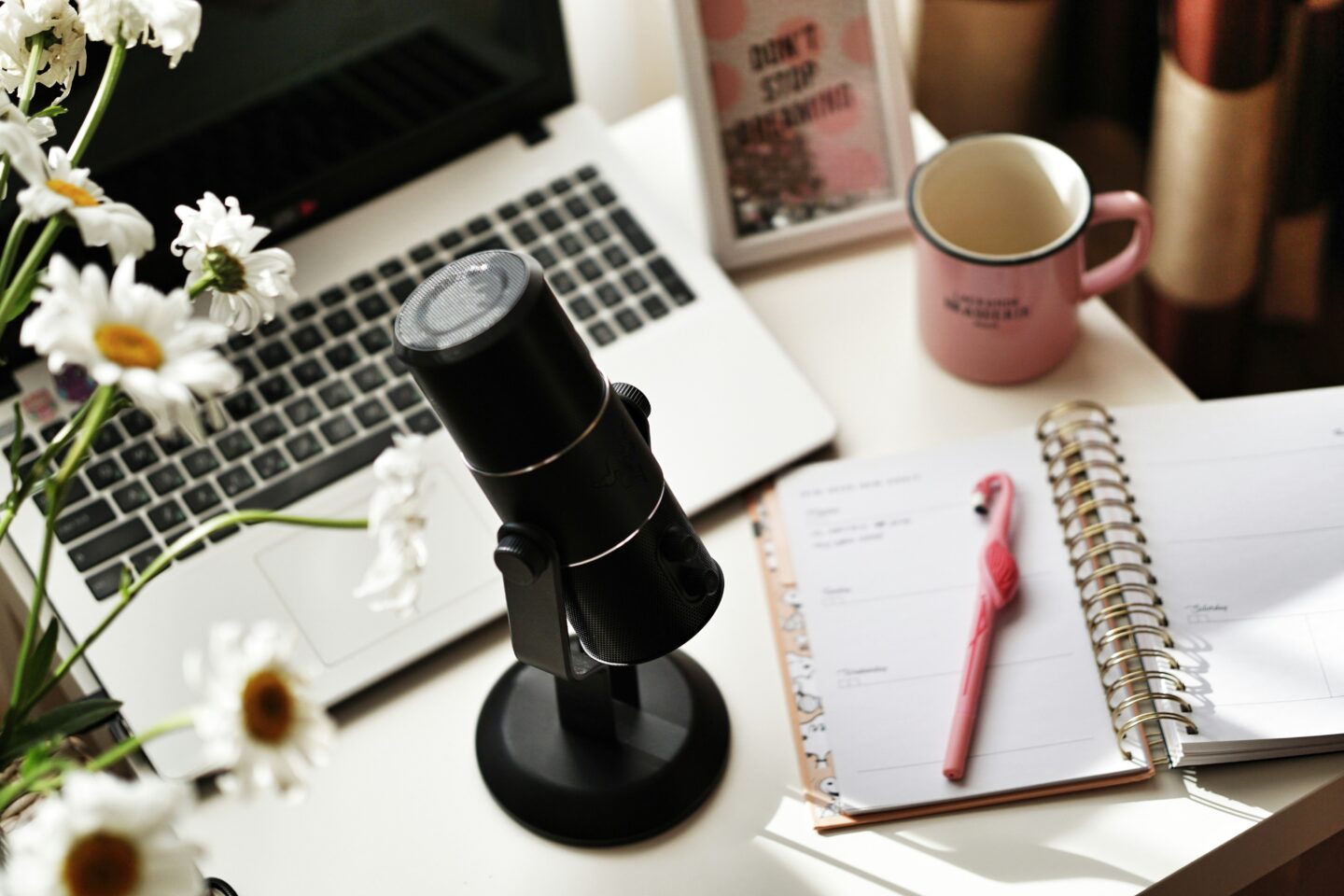 feminine desk set up with microphone, notebook, mug and laptop