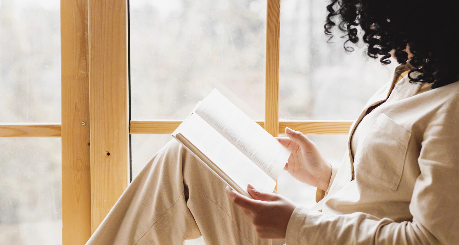 woman holding book sitting in window