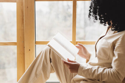 woman holding book sitting in window