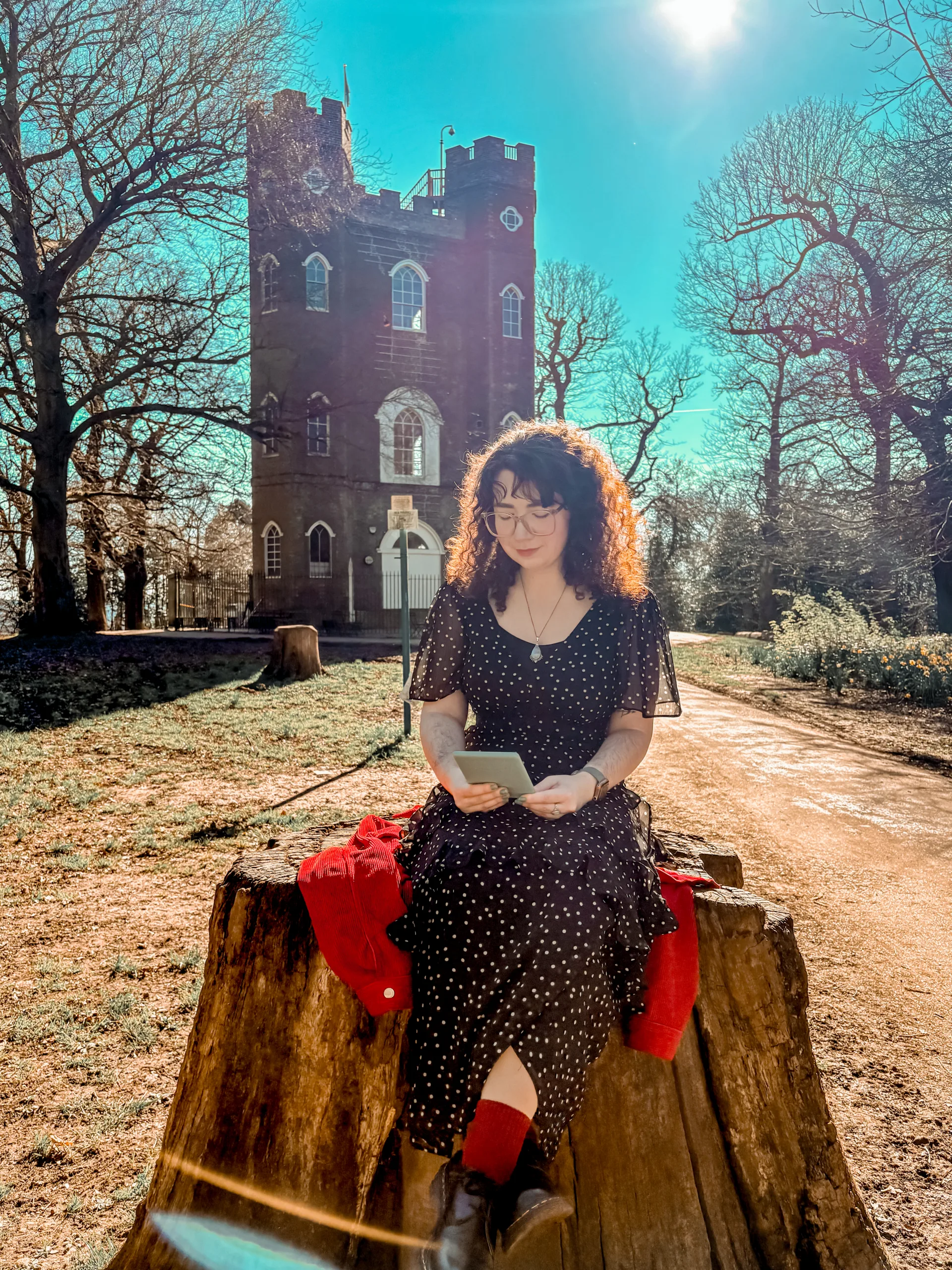 reading kindle sitting on a tree stump in front of a castle
