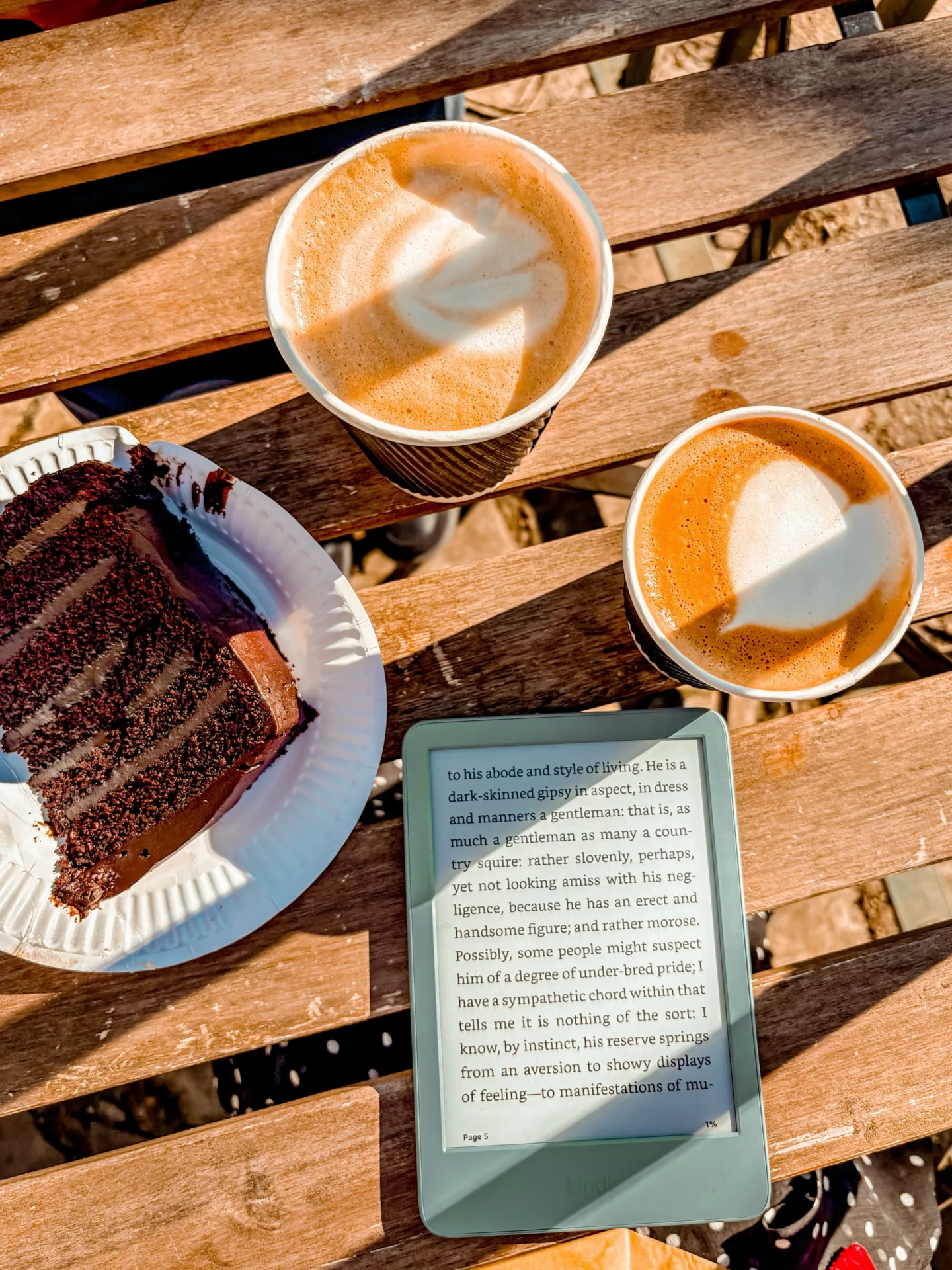 Reading on Kindle at cafe outdoors with coffee and cake.