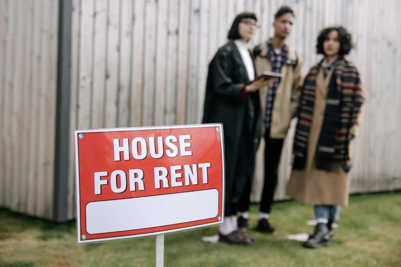 people standing behind house for rent sign